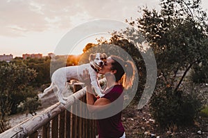 young woman and her cute small jack russell terrier dog watching sunset outdoors in a park. Golden hour. Love for animals concept