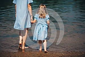 Young woman and her daughter barefoot walk in the water on a river. Back view. Closeup