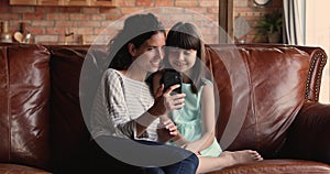 Young woman her daughter relaxing on sofa using smartphone