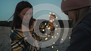 Young Woman And Her Daughter Sit On The Beach With Lights