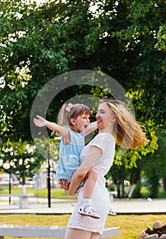 A young woman and her daughter are spinning in their arms. Mom and daughter are laughing and having fun