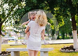 A young woman and her daughter are spinning in their arms. Mom and daughter are laughing and having fun