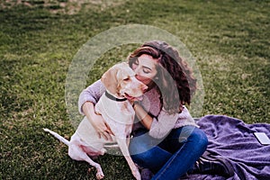 young woman with her dog at the park. she is kissing the dog. autumn season