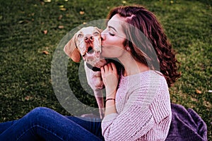 young woman with her dog at the park. she is kissing the dog. autumn season