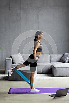 Young Woman during her fitness workout at home with rubber resistance band