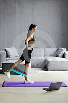 Young Woman during her fitness workout at home with rubber resistance band