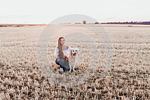 Young woman and her golden retriever dog in a yellow field ar sunset. Pets outdoors