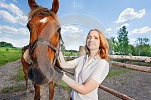Young woman with her horse next to enclosure fence
