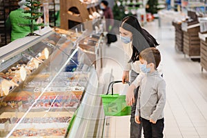 Young woman and her kid wearing protective face masks shop a food at a supermarket during the coronavirus epidemic or