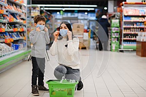 Young woman and her kid wearing protective face masks shop a food at a supermarket during the coronavirus epidemic or
