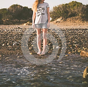 A young woman with her legs naked is standing on the water`s edge