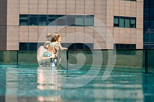 Young woman with her little daughter in the pool on the roof of a skyscraper in a metropolis look overboard