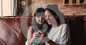 Young woman her little daughter relaxing on couch with smartphone