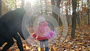 Young woman and her little daughter throw yellow autumn leaves in the city park. Slow motion