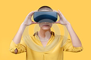 Young woman in her 30s using virtual reality goggles. Woman wearing VR glasses isolated over yellow background. VR experience. photo