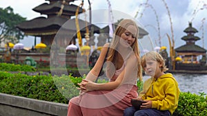 Young woman and her son sitting in front of a Pura Ulun Danu temple on the lake Bratan in Bali, Indonesia