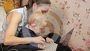 Young woman with her son sitting at home on the couch with a laptop. Look carefully at the screen and press the keys.