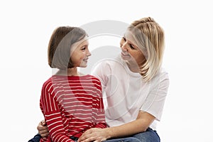 A young woman with her teenage daughter hugs and looks at each other with tenderness. White background