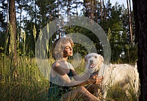 Young woman and her white dog are sitting in the tall grass in the forest