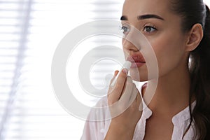 Young woman with herpes applying lip balm against light background. Space for text