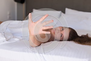 Young woman hides her face from the camera shy and smiling  lying on a bed in the bedroom and covered sheet.