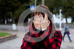 Young woman hides her face in her palms on street background.