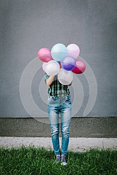 Young woman hiding behind colorful air balloons