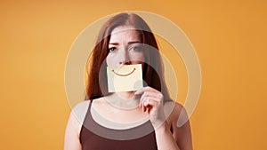 young woman hiding emotion with fake smile drawn on paper