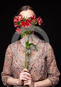 Young woman hiding face behind fresh flowers