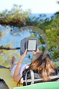 Young woman on hike resting on ground and reading ebook