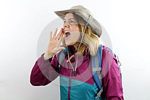 Young woman hiker with hat and backpack shouting and screaming loud to side with hand on mouth.