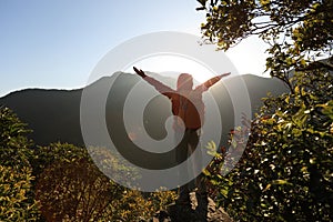 Young woman hiker open arms to sunrise on mountain peak