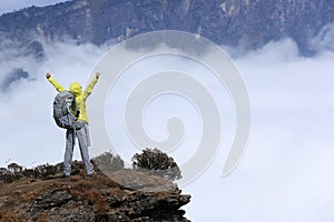 Young woman hiker pen arms on mountain peak