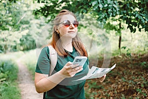Young woman hiker reading map hiking trip looking to find place to go by phone