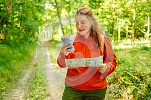 Young woman hiker reading map hiking trip looking to find place to go by phone