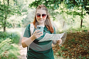 Young woman hiker reading map hiking trip looking to find place to go by phone