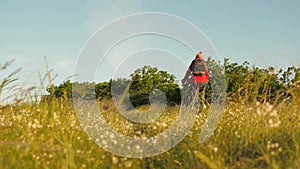 Young woman hiker rides a bicycle on field and grass enjoying nature and fresh air. Free girl travels with bike in