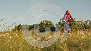 Young woman hiker rides a bicycle on field and grass enjoying nature and fresh air. Free girl travels with bike in