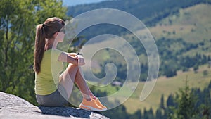 Young woman hiker sitting alone on rocky mountain enjoying view of summer nature on wilderness trail. Active way of life