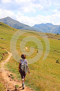 Young woman hiker walks in the high mountain trail in the Italian Alps on the Dolomites mountain range