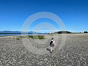 A young woman hiking alone at low tide between Denman Island and Jáji7em and Kw’ulh Marine Park