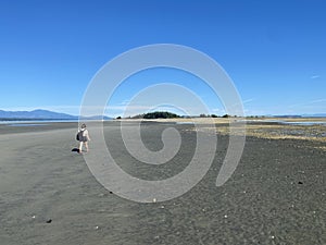 A young woman hiking alone at low tide between Denman Island and Jáji7em and Kw’ulh Marine Park