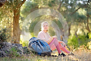 Young woman hiking in countryside. Girl resting under olive tree. Concepts of adventure, extreme survival, orienteering.