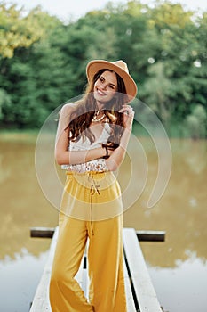 A young woman in a hippie look and eco clothing travels outdoors by the lake wearing a hat and yellow pants in the fall