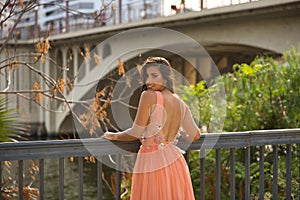 Young woman, Hispanic, beautiful, brunette, wearing an elegant salmon-colored dress, leaning on a railing looking over her