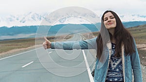 Young woman hitch-hiking on a road at the fields. Young girl hippy hitchhiking on the road. Among the mountains in