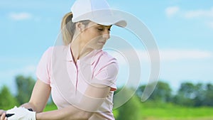 Young woman hitting golf ball confidently holding club in her hands, pastime