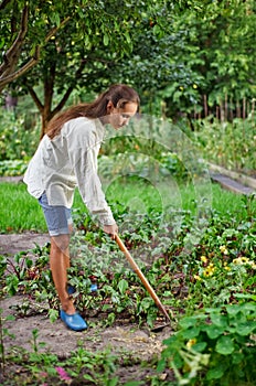 Young woman with hoe working in the garden bed photo