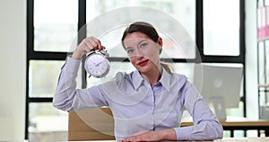 Young woman holding an alarm clock and smiling at camera in office