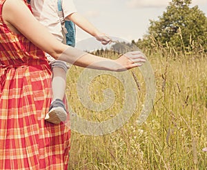Young woman holding baby toddler on her arms walking in the summer meadow